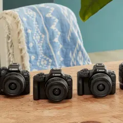 Trzy czarne aparaty Canon EOS z obiektywami i akcesoriami na drewnianym stole.