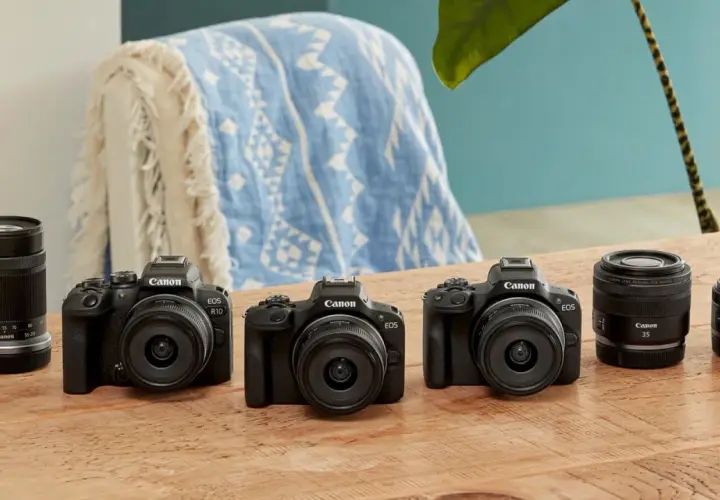 Trzy czarne aparaty Canon EOS z obiektywami i akcesoriami na drewnianym stole.