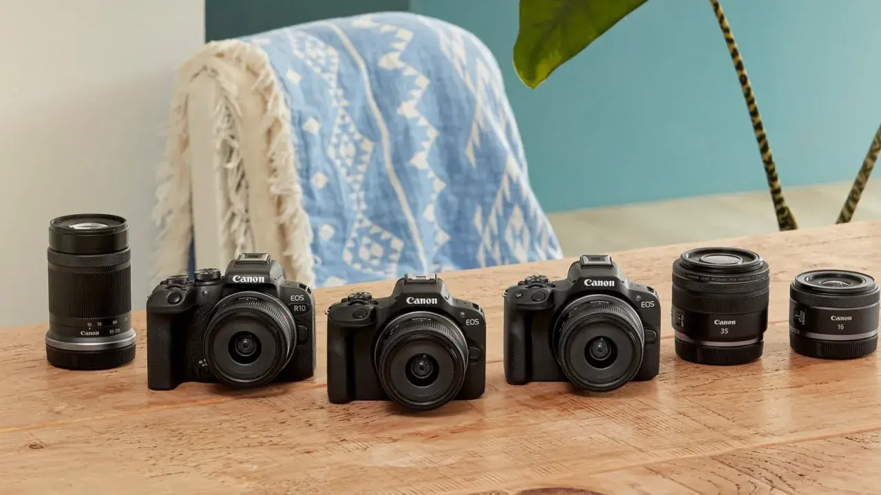 Trzy czarne aparaty Canon EOS z obiektywami i akcesoriami na drewnianym stole.