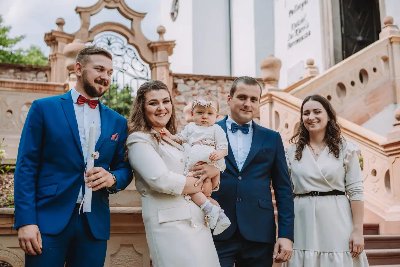 Rodzina pozuje do zdjęcia przed kościołem z dzieckiem na chrzcie. Zastanawiasz się, ile kosztuje fotograf na chrzest?